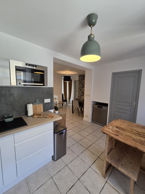 Cuisine moderne et coin repas de l'appartement Residence Cosy à Saint-Méen-le-Grand avec armoires blanches et table en bois