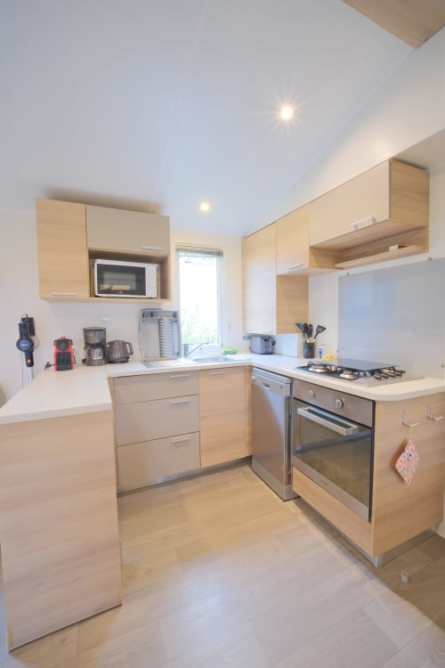 Cuisine moderne du mobil-home Annick à Vias Plage avec armoires en bois clair, appareils inoxydables et blanc