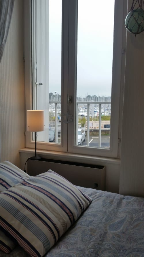 Chambre lumineuse avec linge de lit rayé, lampe de fenêtre et vue sur la marina du balcon à Mer et Maisons, La Trinité sur Mer
