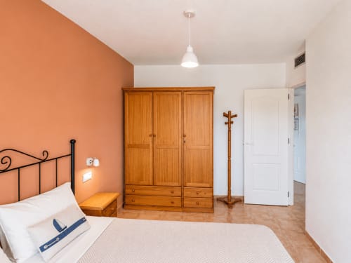 Spacious bedroom at Apartamentos El Calón Playa with orange accent wall, wooden wardrobe, and sea-view apartment in Cuevas