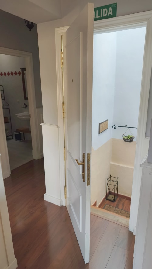 Entrada del pasillo del apartamento Mirador Medieval en Cáceres con puertas blancas, señal de salida y vista de escaleras
