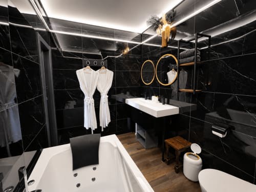 Salle de bain luxueuse aux carreaux de marbre noir, baignoire blanche, finitions dorées et vasque de vanité au Domaine Valenquercy