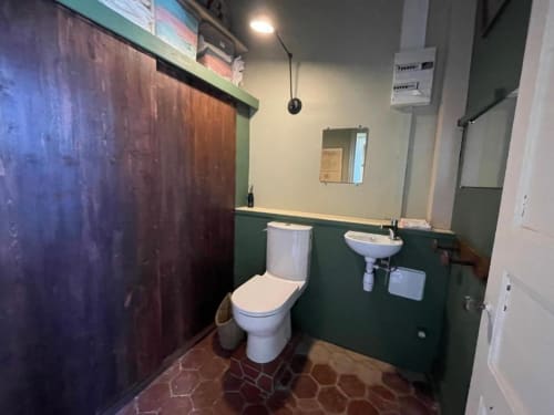 Salle de bain du Château de Vaux Morvan avec murs verts, toilettes blanches, lavabo et carrelage en terre cuite à Étang sur Arroux
