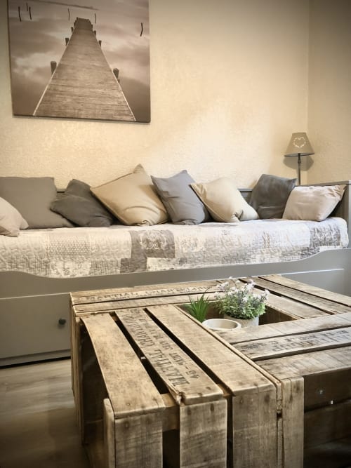 Salon douillet avec table basse en palettes, canapé confortable aux coussins neutres et tableau de pont à Le Paillot