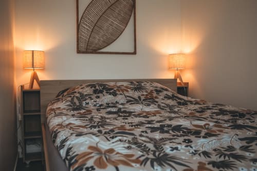 Chambre chaleureuse du cottage Les Tropiques à ART DE VOYAGER, Étretat, avec parure florale, lit en bois et ambiance douillette au chevet