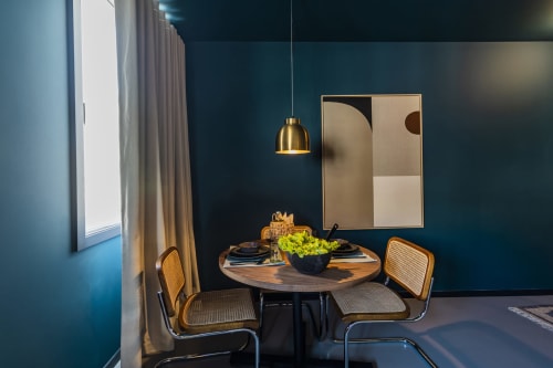Sala de jantar moderna em hotel do Porto com mesa redonda de madeira, cadeiras de rattan, pendente de latão, paredes azul-petróleo e decoração abstrata