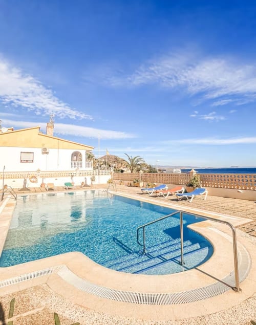 Swimming pool at Apartamentos El Calón Playa with sea view, lounge chairs, and Mediterranean coastline in Cuevas del