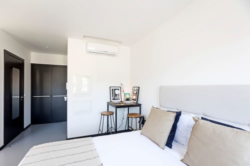 Moderno quarto estúdio compacto em hotel no Porto com cama branca, guarda-roupa preto, escrivaninha e ar condicionado