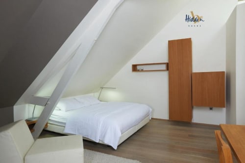 Contemporary attic bedroom at Hidden Bay Hotel with white walls, wooden wardrobe, bed with white linens, and hardwood