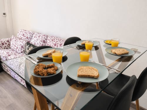 Mesa de desayuno en Apartamentos El Calón Playa con galletas, tostadas, zumo de naranja y cubiertos para los huéspedes.