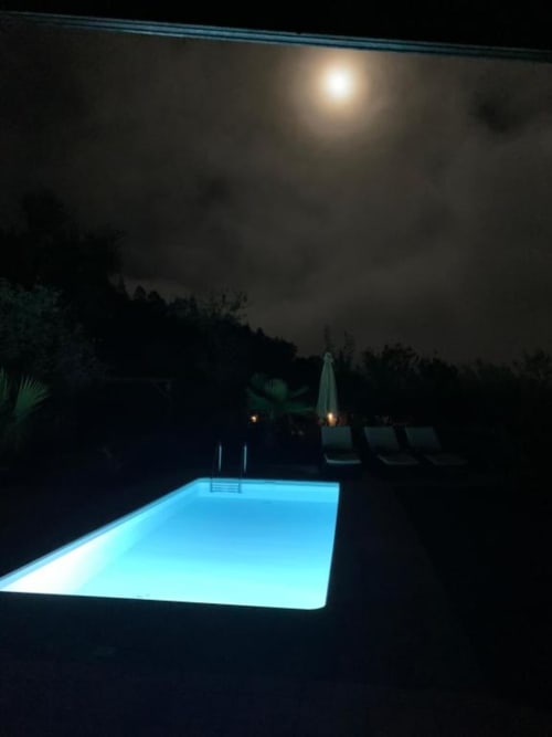 Vista nocturna iluminada de la piscina privada de Villa El Topo, La Palma, con tumbonas y paisaje ajardinado bajo la luz lunar