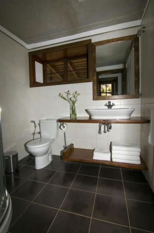 Baño moderno en villa Rural La Palma con lavabo tipo vessel, mueble de madera, azulejos blancos, piso oscuro y detalles decorativos