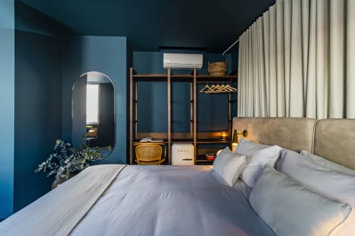 Quarto moderno no hotel Benefit Collection Porto com paredes azul-piscina, cabeceira estofada bege, guarda-roupa de madeira, espelho redondo