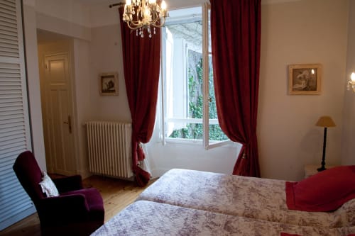 Chambre élégante aux Pratges B&B à Figeac avec lits jumeaux, rideaux bordeaux, lustre en cristal et vue sur le jardin