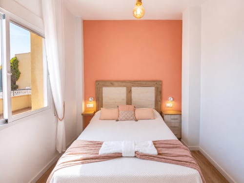 Modern coral bedroom with wooden headboard, white bedding, and sea view window in Cuevas del Almanzora apartment