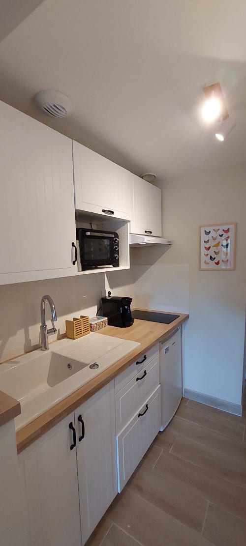 Modern kitchen in Sunflowers cottage at Les Gites de Campardon with white cabinets, wooden counter, sink, and mini-oven
