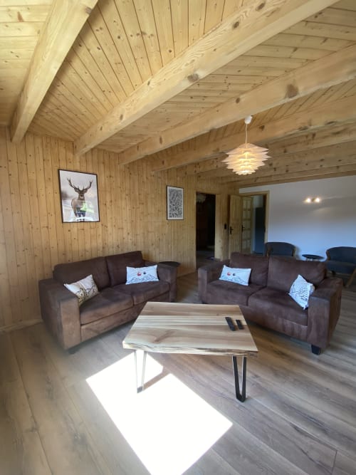 Modern wooden chalet living room with two brown sofas, wooden ceiling beams, and mountain lodge decor at La Ferme des