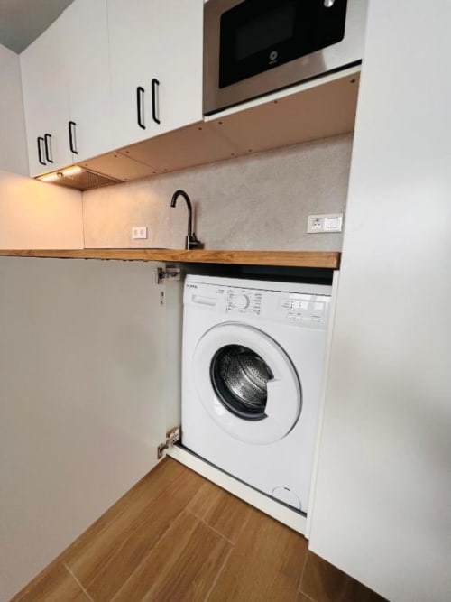 Cocina moderna con lavadora blanca bajo encimera de madera, horno de acero inoxidable y armarios blancos en La Palma