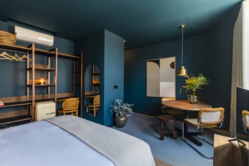 Estúdio de hotel moderno no Porto com paredes azul-esverdeado, móveis em madeira, espaço de trabalho, cama e design contemporâneo