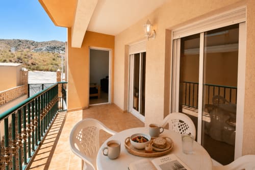 Terraza soleada en Apartamentos El Calón Playa con mesa de desayuno, sillas blancas y vistas a las montañas en Cuevas del Almanzora