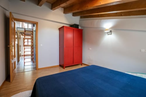 Dormitorio espacioso en apartamento de Montgat con cama azul, armario rojo, vigas de madera y vistas a la montaña