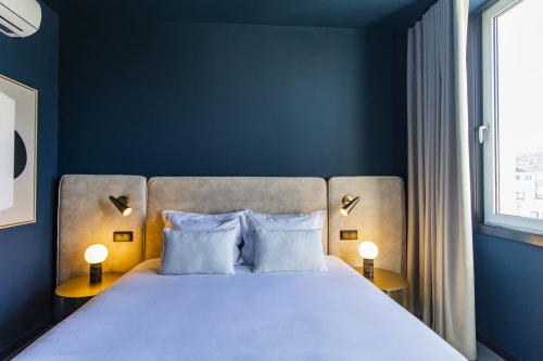 Quarto de estúdio moderno e compacto no Benefit Collection Porto com paredes azuis, cabeceira estofada e iluminação de criado.