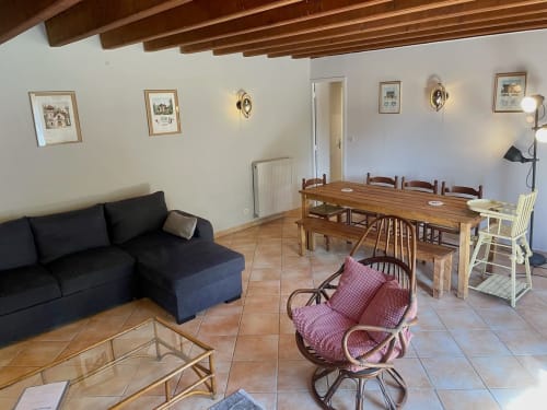 Salon lumineux avec coin repas, canapé noir, table en bois et vue sur le jardin au Château de Vaux Morvan