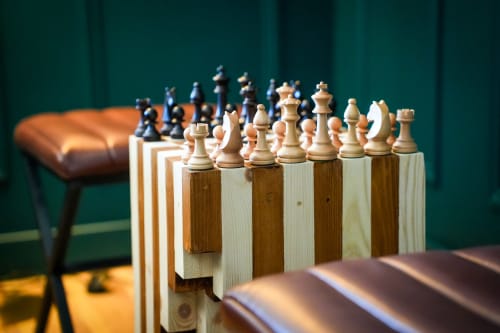 Pièces d'échecs sur socles en bois dans l'appartement Les séjours Ardennais Escapade Chic à Renwez, avec fauteuil cuir et mur vert