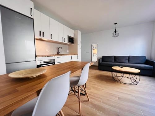 Cocina y salón de planta abierta con mesa de madera, sillas blancas, sofá oscuro y acero inoxidable