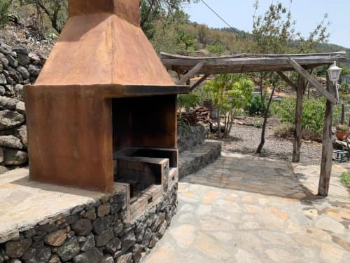 Rústica zona de barbacoa al aire libre con horno de terracota en Villa El Topo, La Palma, con pérgola de madera y jardín de montaña