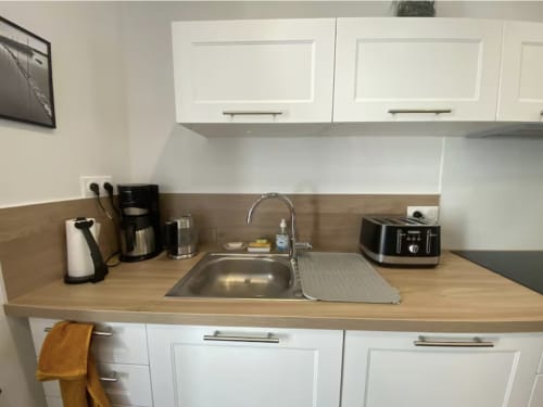 Kitchenette compacte au 58 Bayeux avec placards blancs, plan de travail en bois, évier et petits électroménagers incluant cafetière