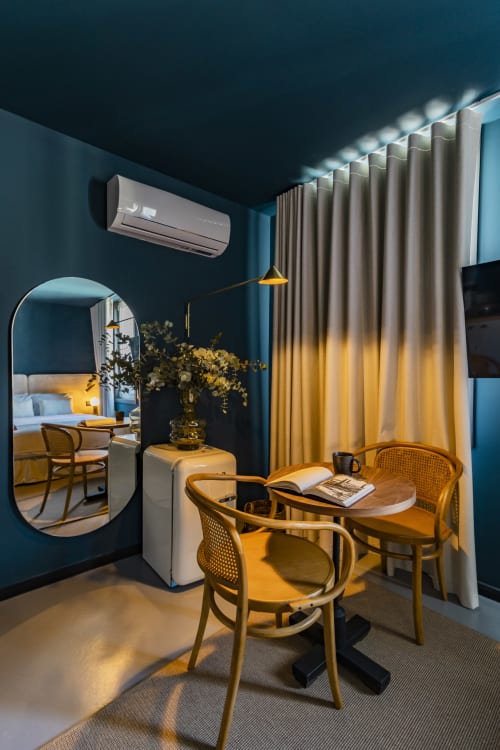 Estúdio de hotel moderno no Porto com paredes azul-petróleo, mesa de madeira, cadeiras de vime e iluminação aconchegante na área de jantar