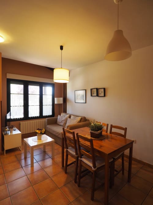 Acogedor departamento de 1 dormitorio con comedor de madera, sofá, iluminación colgante y vistas al jardín en Senda Rural