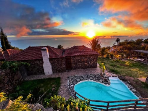 Villa Awara al atardecer con piscina turquesa, arquitectura de piedra, horizonte oceánico y jardín tropical en La Palma