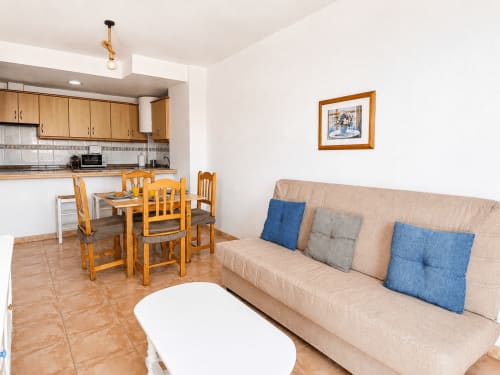 Spacious living area in Apartamentos El Calón Playa with beige sofa, wooden dining table, and open kitchen in Cuevas del