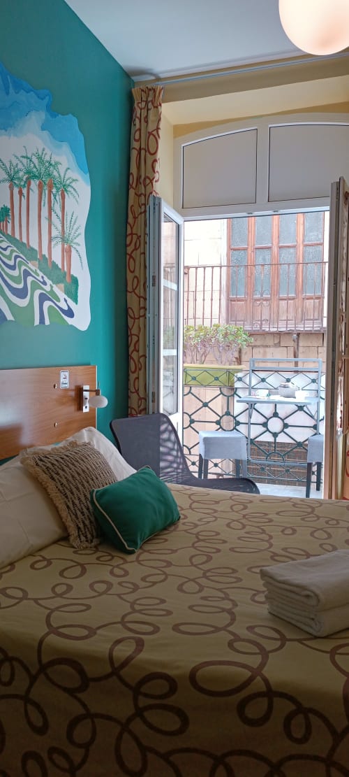 Habitación moderna en Pensión Alicante San Nicolás con pared turquesa, ropa de cama estampada y balcón con vistas a la ciudad