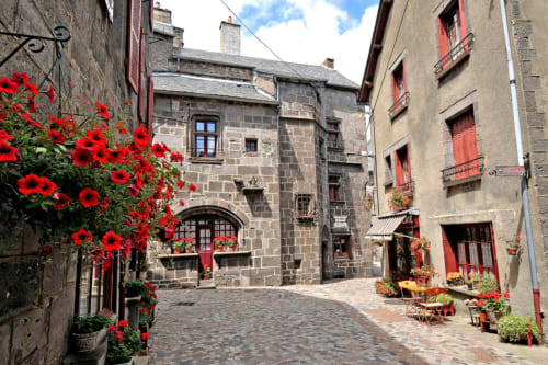 Cour pavée de charme à Bergerac avec fleurs rouges, bâtiments historiques en pierre et volets rouges au Relais de La