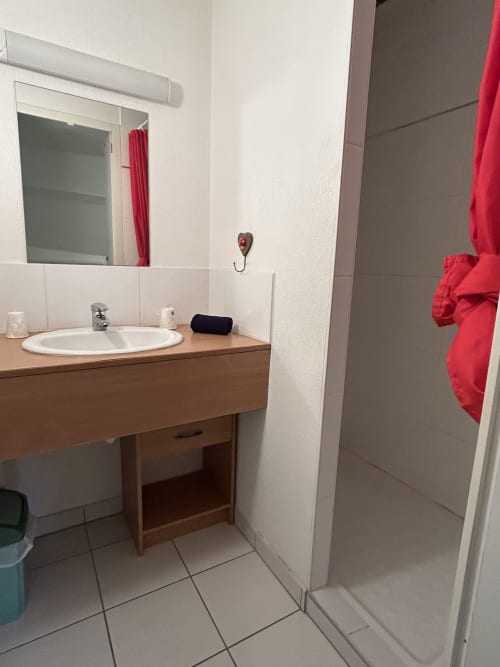 Salle de bain moderne à Hébergement Luxeuil Les Bains avec meuble-lavabo en bois, lavabo rond, miroir, douche et serviettes rouges