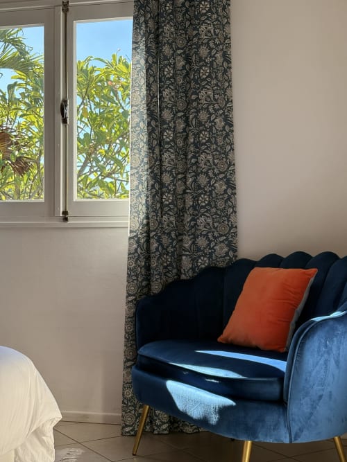 Élégante chambre de La Villa Maraloupia avec fauteuil en velours bleu, coussin orange et vue sur la mer par les portes vitrées