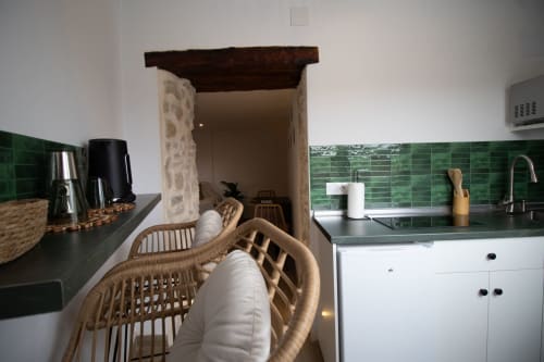 Moderne Küche mit grüner Fliesenwand, weißen Schränken und Flechtsessel in einem Loft in Setenil de las Bodegas