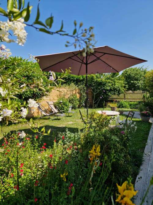 Jardin fleuri aux Chambres du Keriolet avec parasol marron, transats et fleurs colorées à La Trinité-sur-Mer
