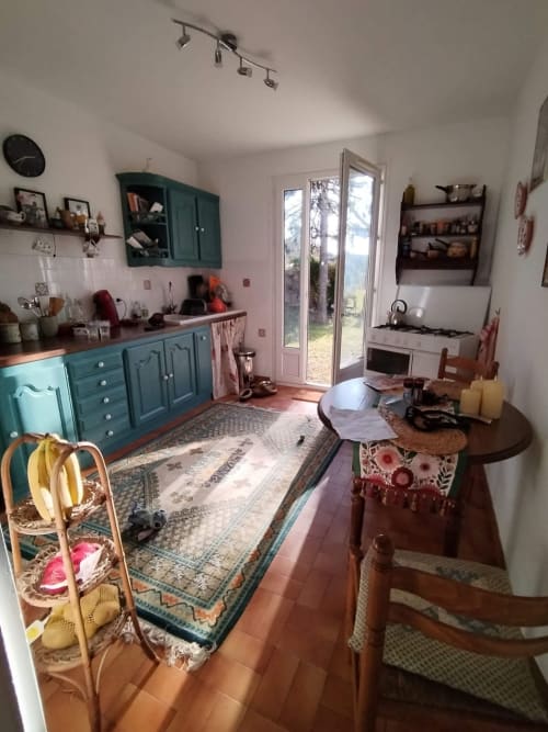 Bright kitchen and dining area in dog-friendly villa near Nyons with teal cabinets, terracotta tiles, and garden view through