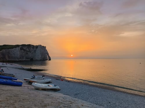 Coucher de soleil sur la plage d'Étretat avec falaises blanches, bateaux de pêche et mer calme au gîte ART DE VOYAGER