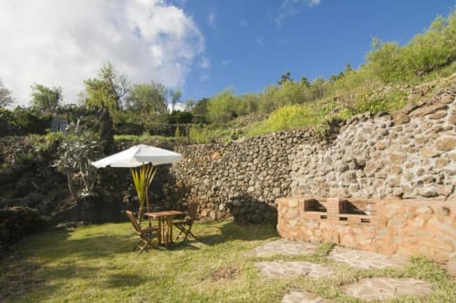 Terraza de Villa Awara con sombrilla blanca, muros de piedra y vistas al jardín en El Pinillo, La Palma rural