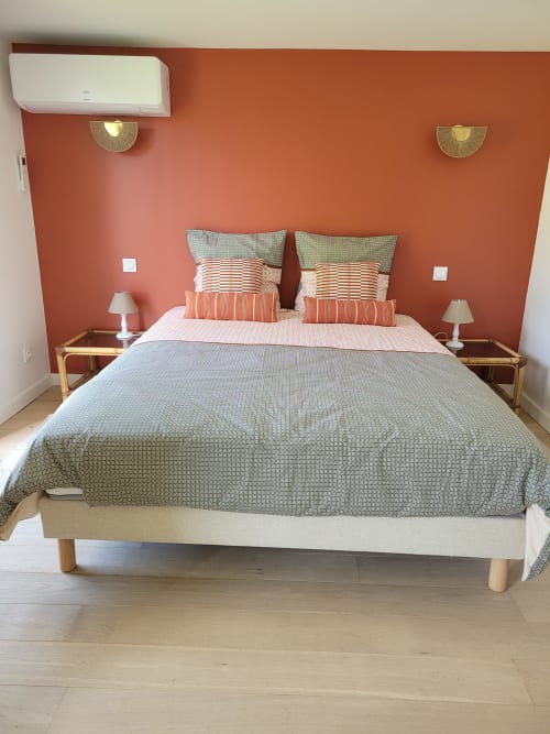 Chambre moderne aux murs corail, lit queen avec coussins rayés, tables de nuit en bois et climatisation au Logis de