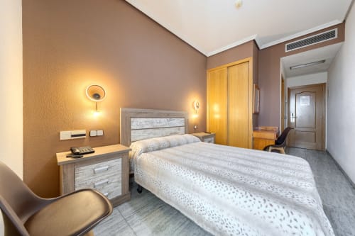 Moderna habitación de hotel en Hostal El Molino con cama matrimonial, muebles de madera, iluminación cálida y vistas a las montañas de Collado