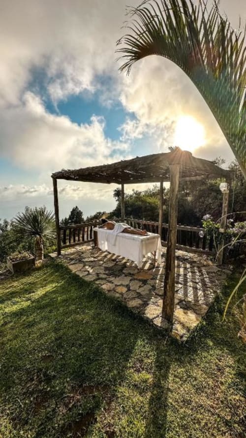 Terraza de comedor al aire libre con pérgola en Villa Awara, vistas al océano, palmeras y paisaje montañoso bajo cielo despejado