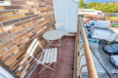 Área de descanso en el balcón del Hostal El Molino con silla blanca, mesa, pared de ladrillo y vistas a las montañas de Collado Villalba