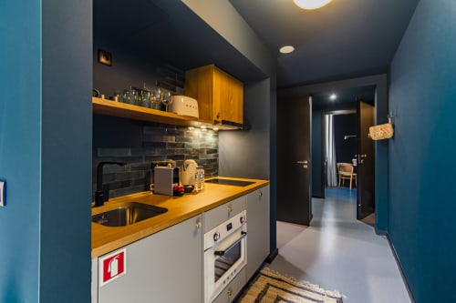 Kitchenette moderna em apartamento de hotel no Porto com bancada de madeira, armários brancos, azulejo escuro e forno em aço inoxidável
