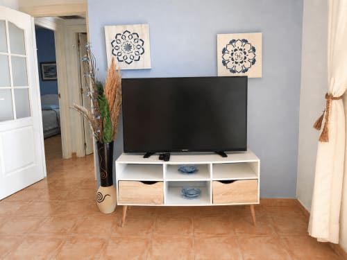 Modern living room with flat-screen TV on white media console, decorative wall art, and terracotta flooring in Apartamentos